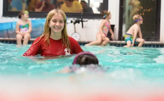 A Swimsational instructor in the pool with young swimmers seated along the wall