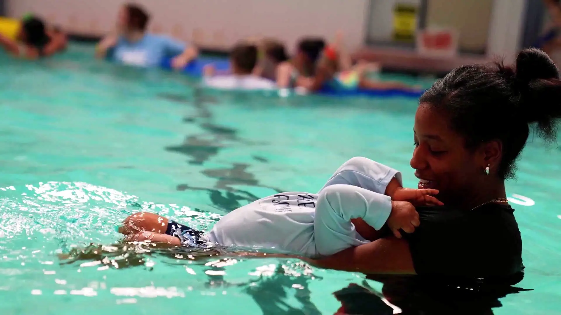 An instructor supports a young swimmer floating on their back